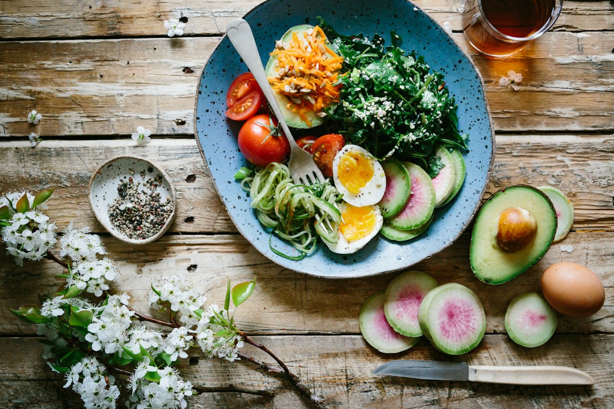 Schale mit Ei, Spinat, Tomaten und Gemüse auf einem Holztisch