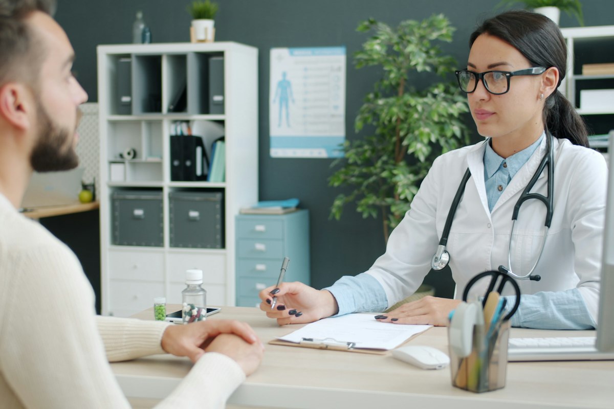 Eine Ärztin spricht an ihrem Schreibtisch mit einem Patienten