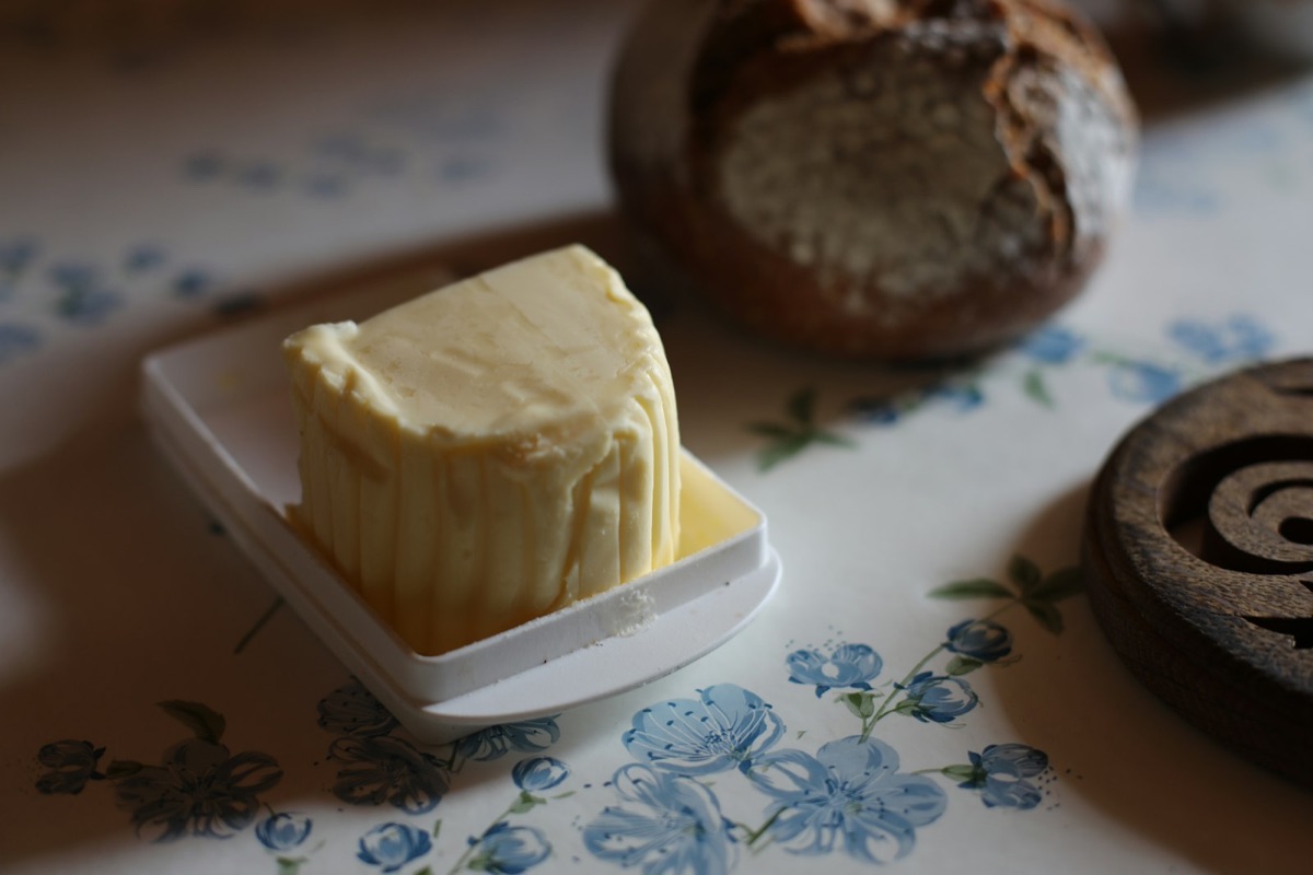 Ein Stück Butter auf einem weißen Teller, daneben Brot