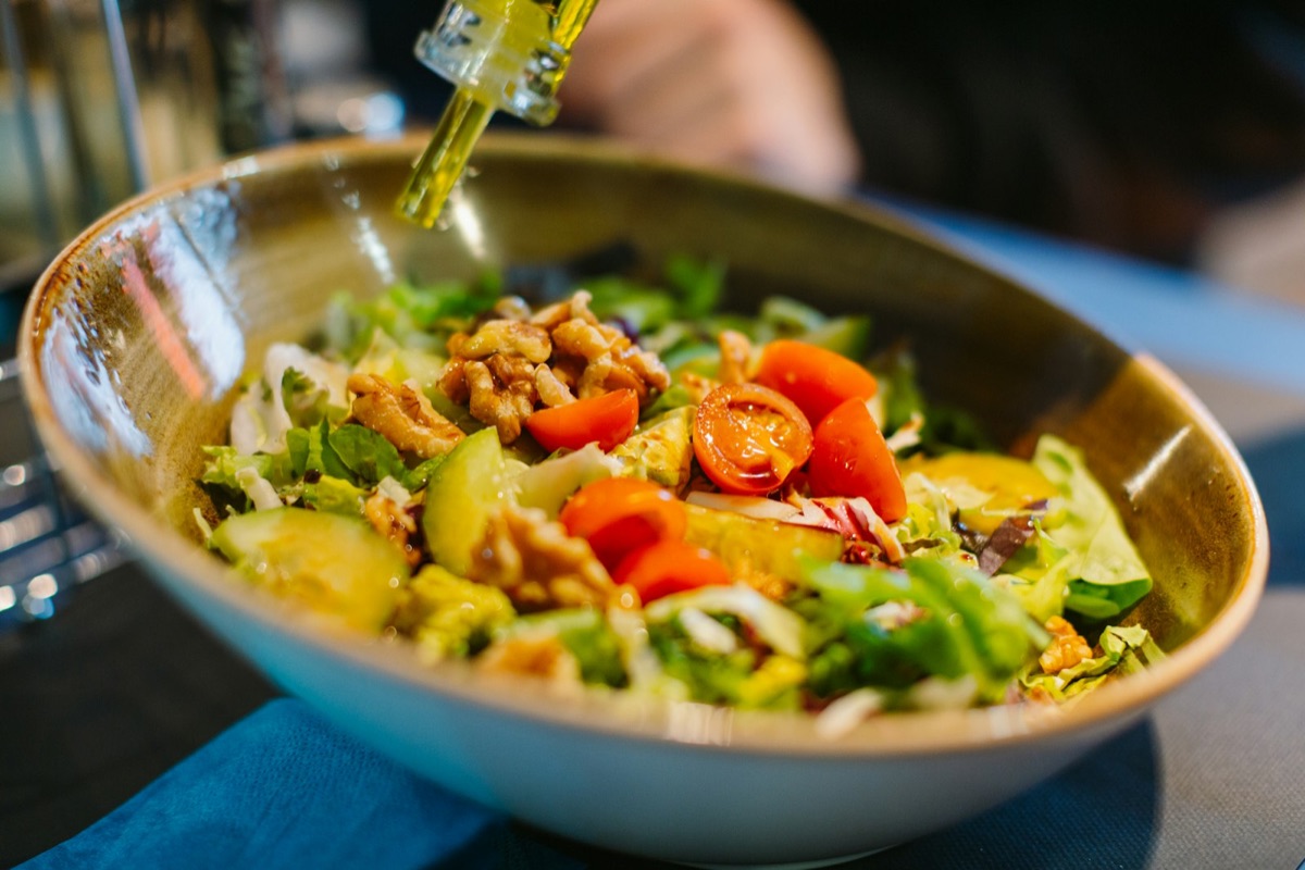 Öl wird über eine Salatschüssel mit Walnüssen und Tomaten geträufelt