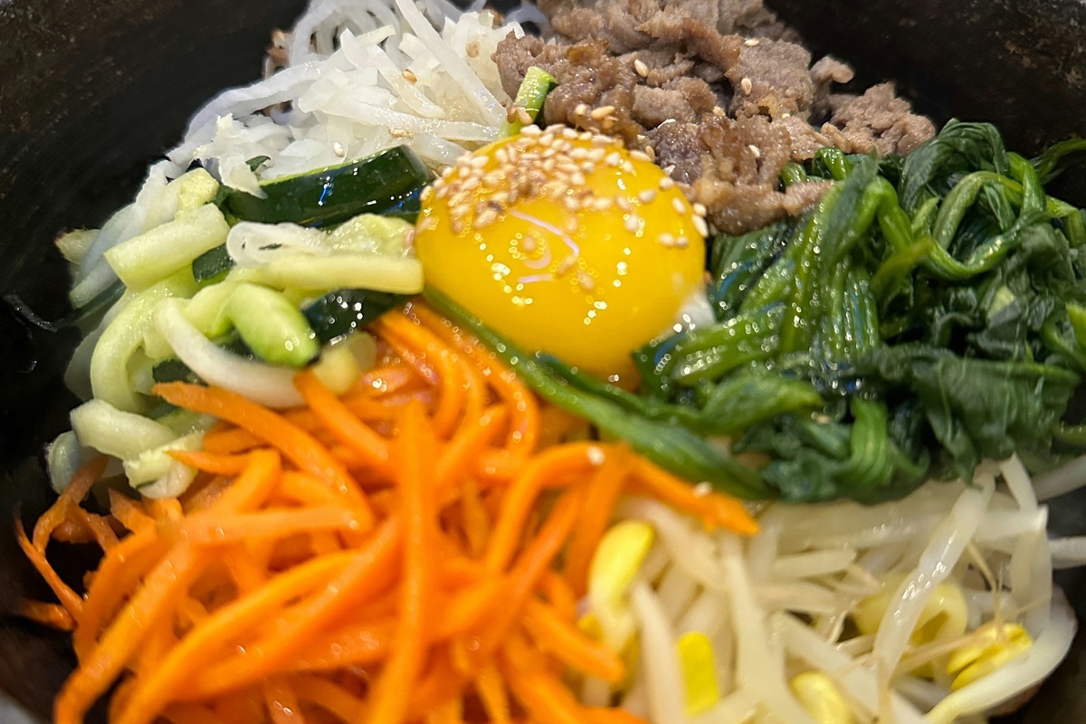 Bibimbap in einer Steinschale mit Eigelb, Möhre, Spinat, Sojasprossen, Gurke und Rindfleisch
