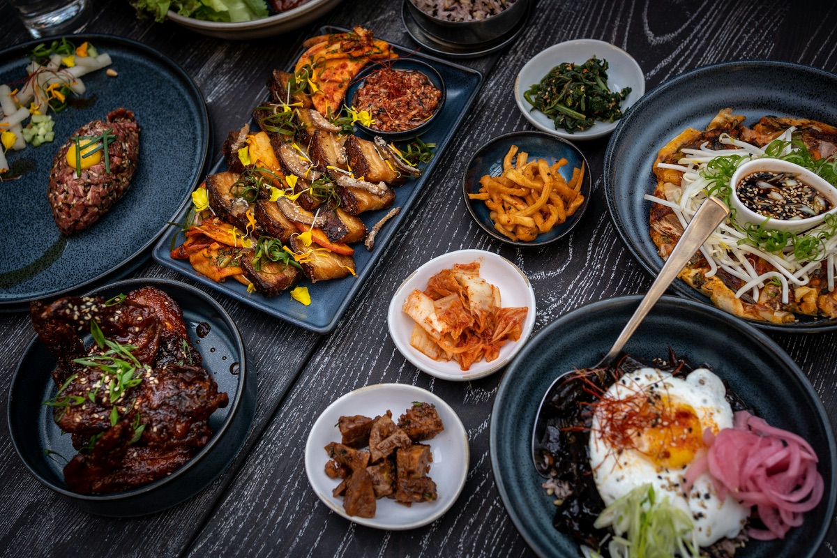 Koreanische Gerichte mit vielen kleinen Beilagen, Kimchi und Bibimbap auf einem dunklen Holztisch