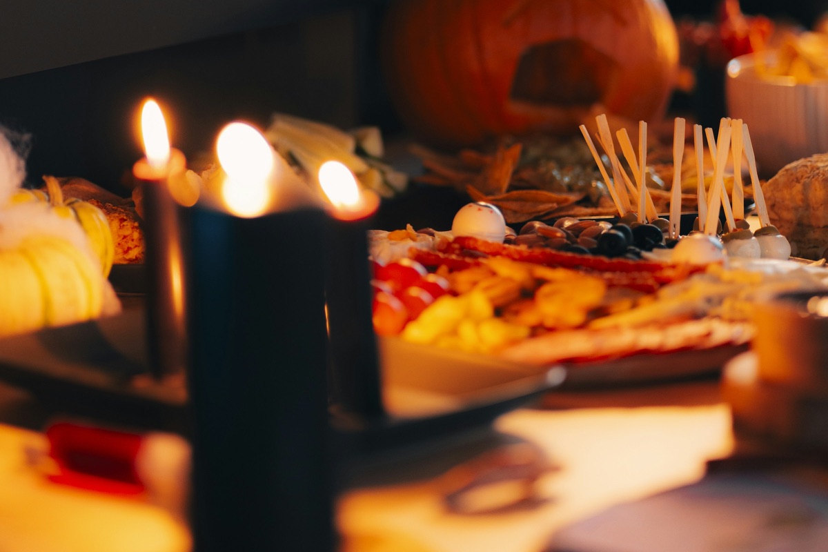 Schwarze Kerzen brennen vor einem Halloween-Buffet mit Fingerfood, dahinter ein geschnitzter Kürbis