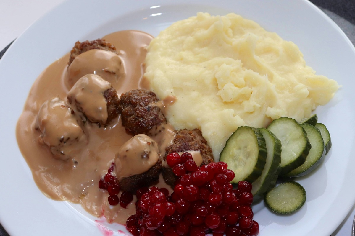 Köttbullar mit Rahmsoße, Kartoffelpüree, Gurkenscheiben und Preiselbeeren auf einem Teller