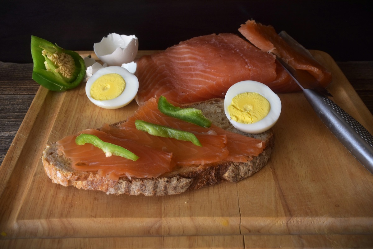 Räucherlachs auf Roggenbrot mit gekochtem Ei auf einem Holzbrett
